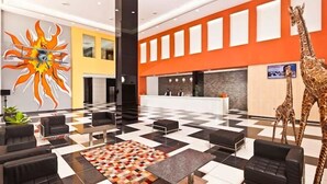 A hotel lobby with a checkered floor, black leather sofas, a colorful rug, a reception desk, and a giraffe statue. - Wonderla Resort (Ramanagara)