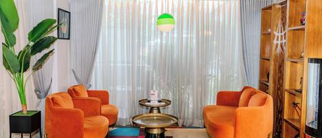 A modern living room with orange armchairs, a round coffee table, and a large potted plant.