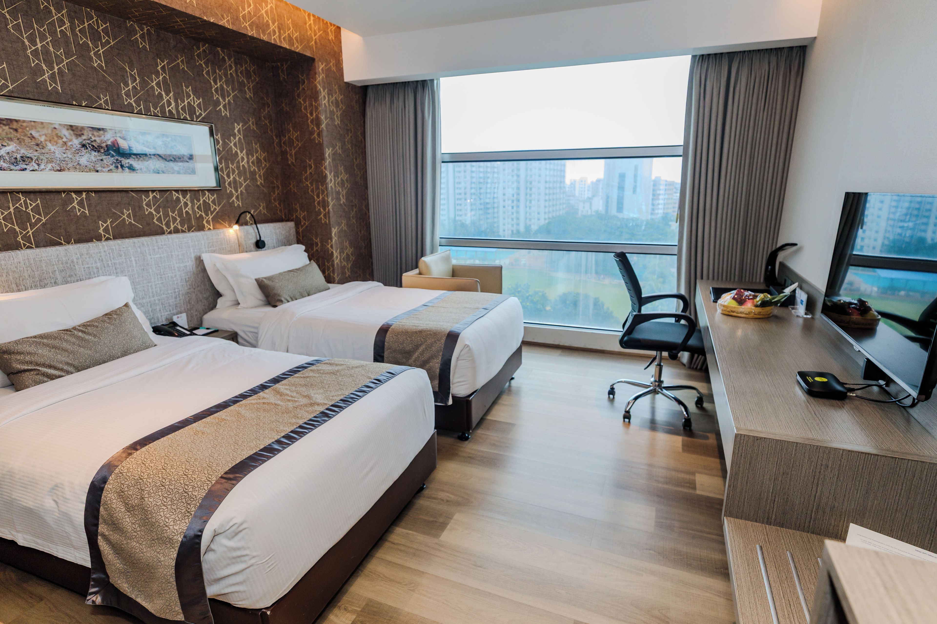 Une chambre d’hôtel avec deux lits, un bureau, une chaise et une grande fenêtre donnant sur la ville.