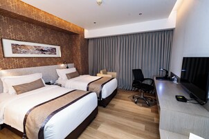 Habitación de hotel con dos camas, un escritorio, una silla, un televisor y un ventanal con cortinas.
