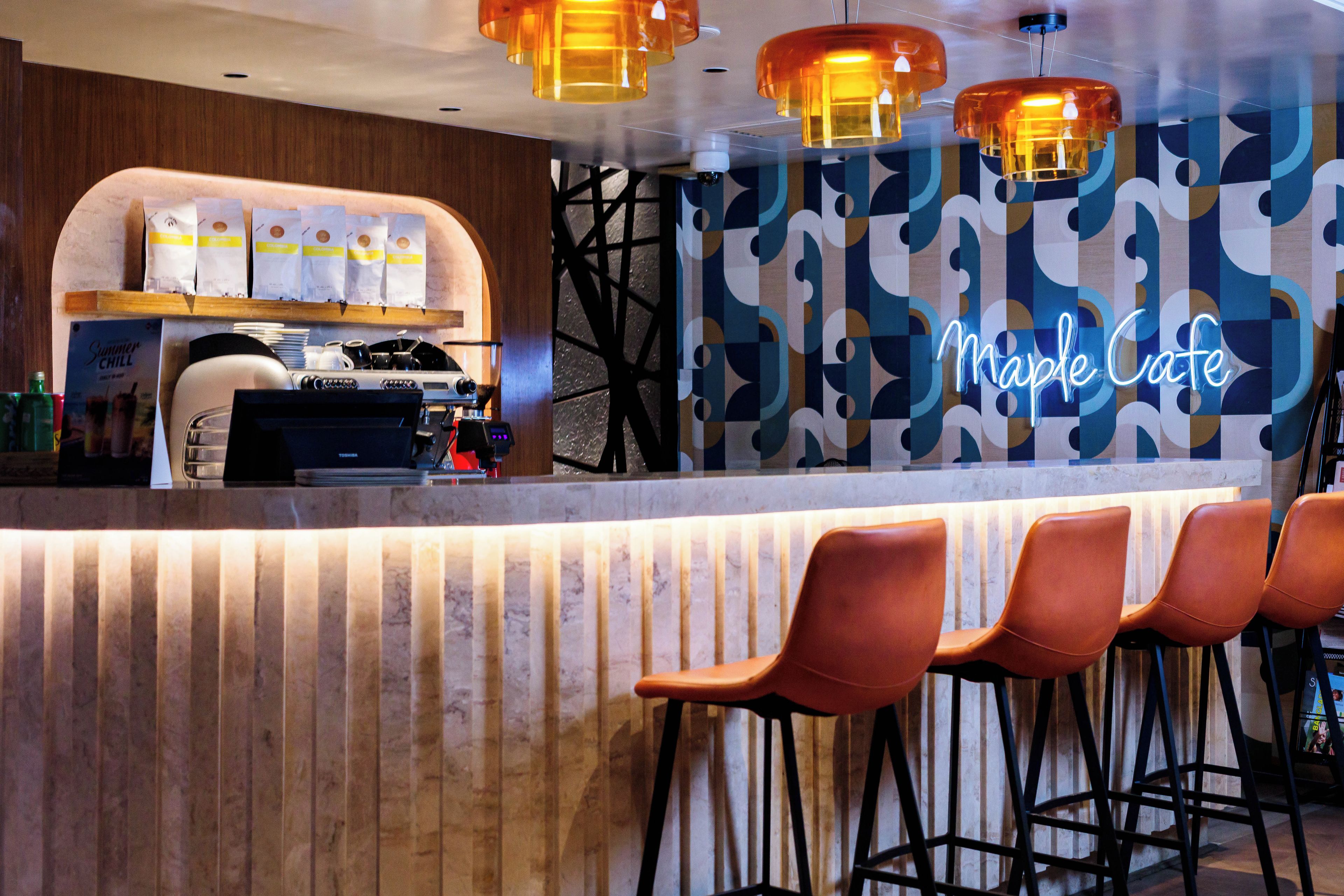 Un espace bar agrémenté d’un panneau néon indiquant « Maple Cafe », d’une machine à café et de tabourets de bar.