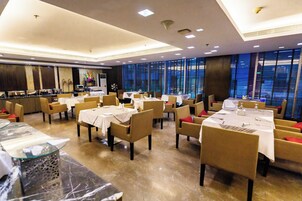 Un restaurante con varias mesas y sillas, una zona de bufé y amplias ventanas.