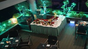 Un área de comedor al aire libre con una mesa preparada para dos personas, rodeada de sillas e iluminada por una luz ambiental verde.