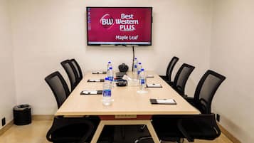 A conference room with a long table, black chairs, a mounted TV displaying 'Best Western PLUS Maple Leaf', and water bottles on the table.
