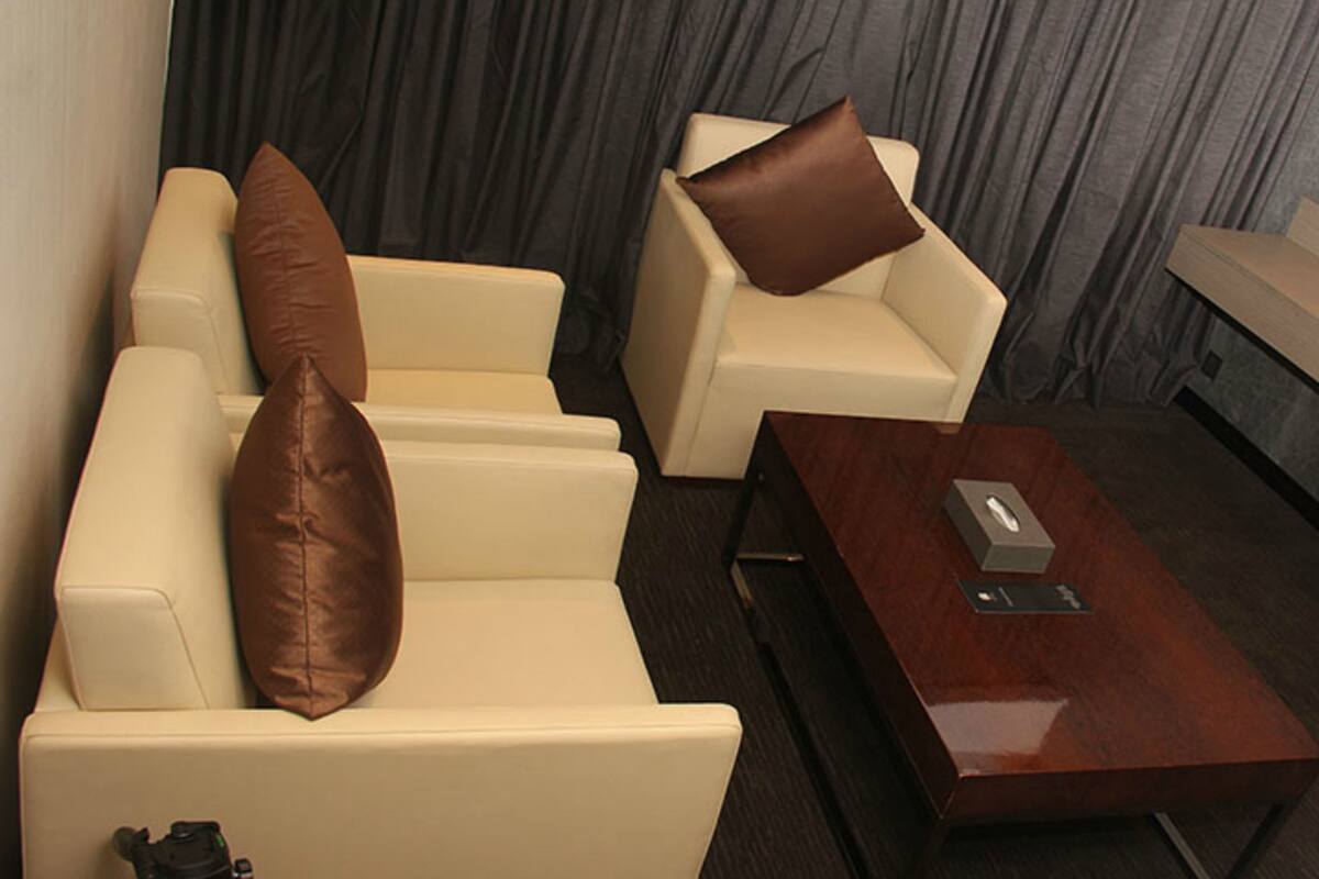 Quarto de hotel com sofá, mesa de centro e cortina ao fundo.