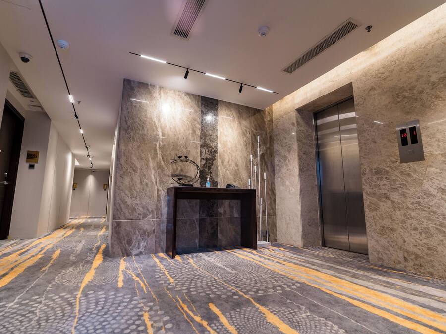 A modern elevator with a digital display, a marble wall, and a patterned carpet.