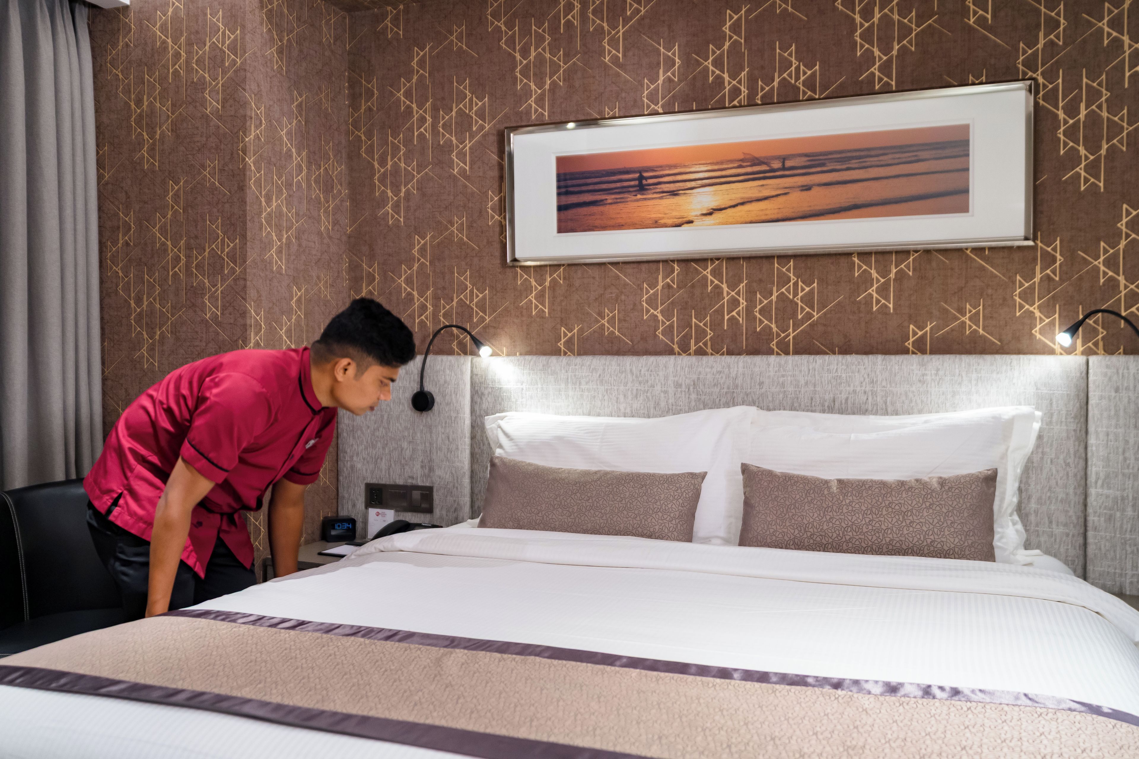 A hotel room with a bed, a nightstand, a clock, and a wall with a geometric pattern.