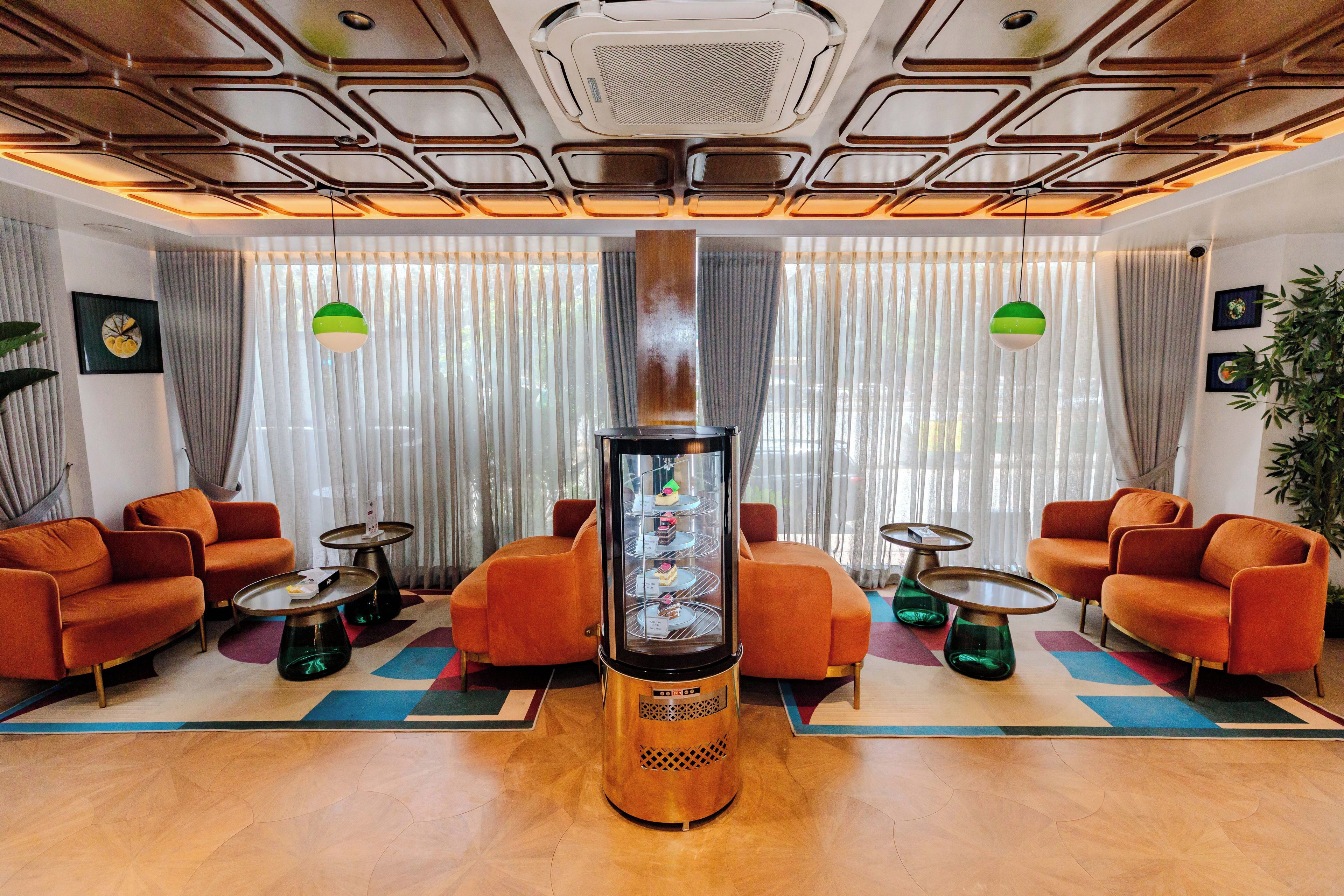 Un vestíbulo moderno con sofás naranjas, una máquina de café central y un techo con diseño.