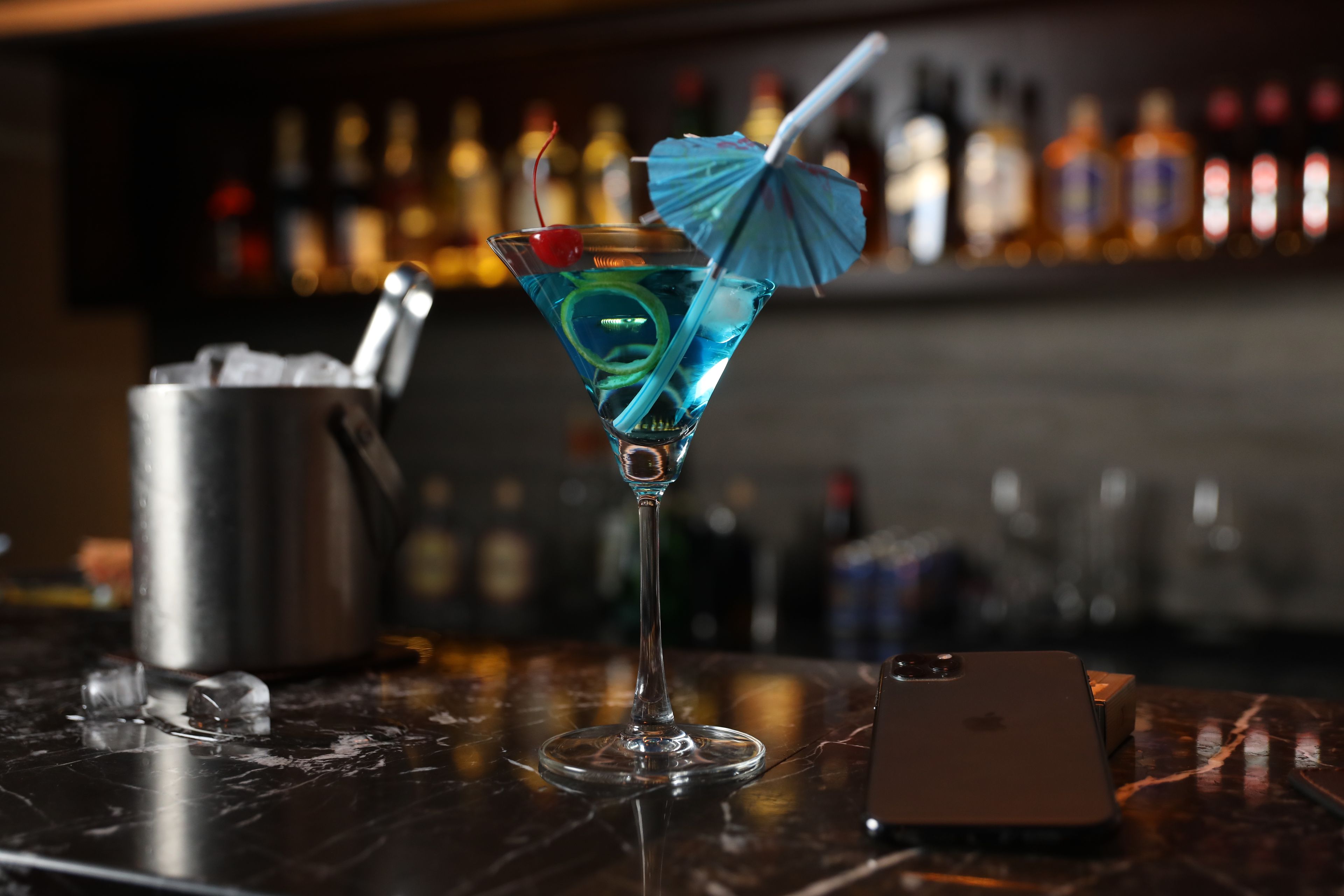 Una copa de martini con un paraguas azul y una cereza sobre la barra.