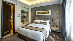 Una habitación de hotel moderna con una cama grande, una mesita de noche con lámpara, un cabecero con altavoces integrados y una obra de arte colgada en la pared.