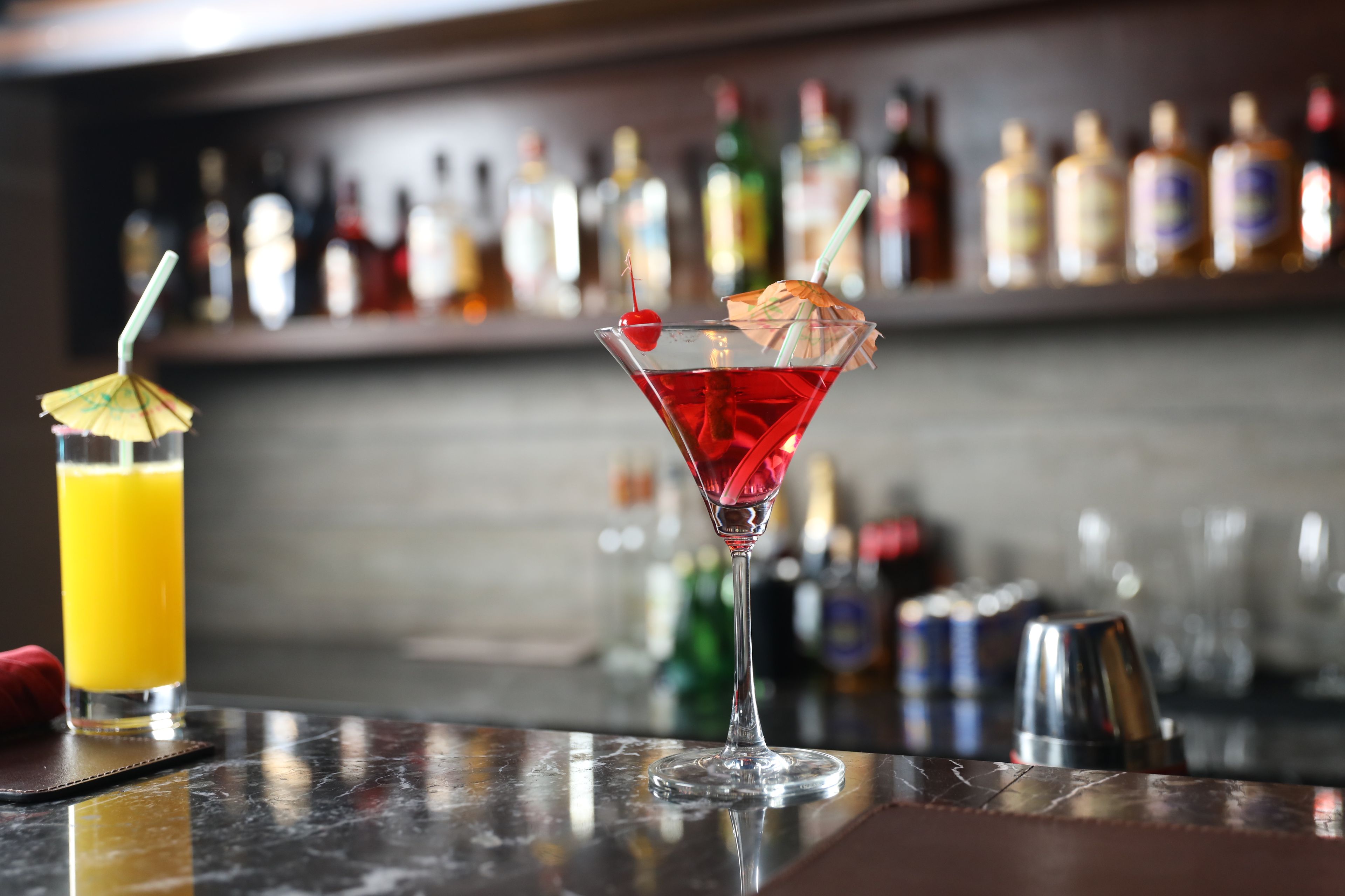 A bar setting with a martini glass and a cocktail with a cherry and umbrella garnish.