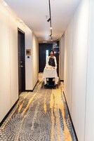 A hotel corridor with a service cart, a door with a room number sign, and a wall-mounted light fixture.