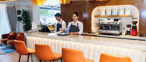 A bar area with orange chairs, a coffee machine, and two baristas.
