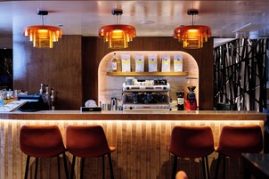 A bar area with a wooden counter, bar stools, and a coffee machine.