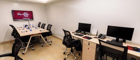 A conference room with a large table, chairs, a TV screen, and multiple computer monitors.