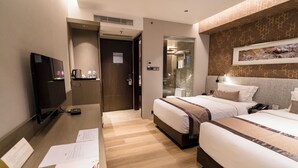 Una habitación de hotel con dos camas, un escritorio con televisor y zona de ducha.