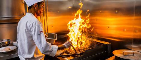 A chef cooking with a large flame on a grill in a stainless steel kitchen.