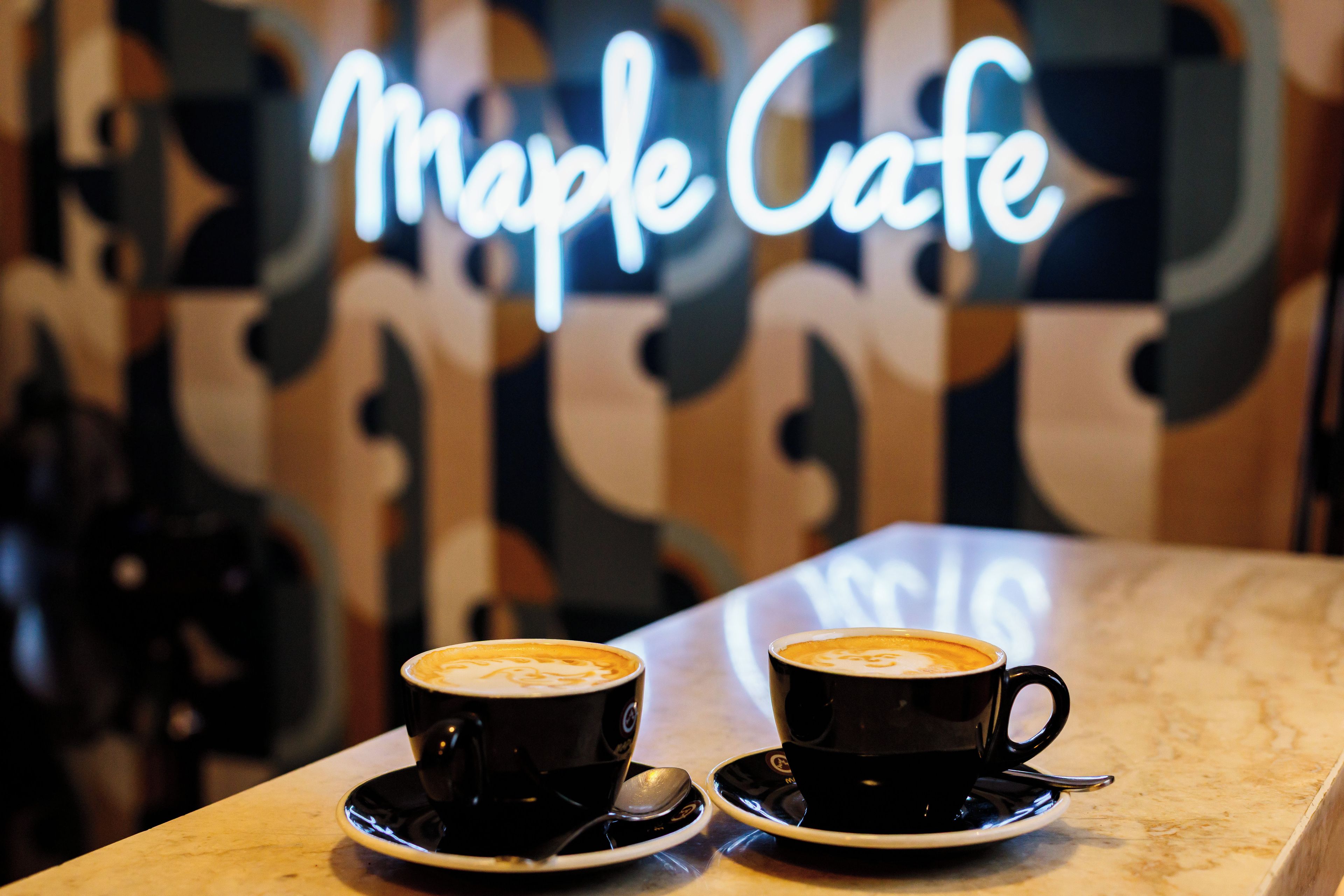 Two cups of coffee on a table with a neon sign in the background.