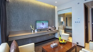 Un moderno vestíbulo de hotel con un televisor de pantalla plana, una recepción, una mesa de centro con frutero y una escalera que conduce al baño.
