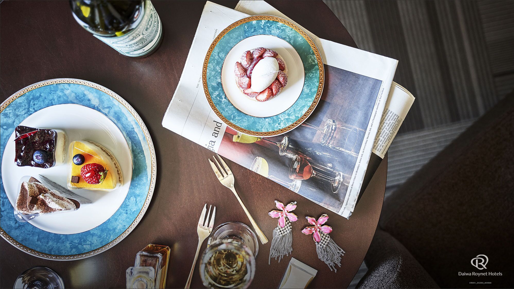 A table set with plates of desserts, a wine glass, cutlery, and a magazine.