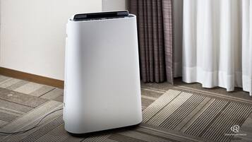 Um purificador de ar branco e portátil num quarto com carpete e cortinas.