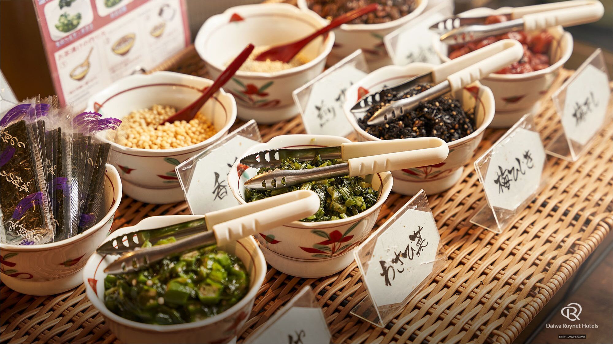 A variety of dishes in traditional bowls with chopsticks and labels, displayed on a woven mat.