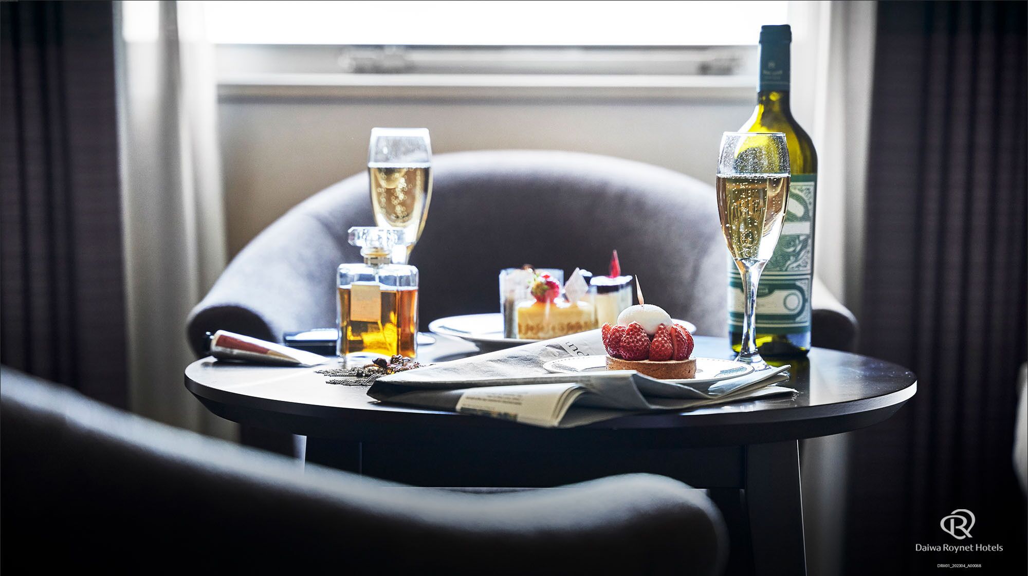 A table with a bottle of wine, two glasses of champagne, a dessert with strawberries, and a candle.