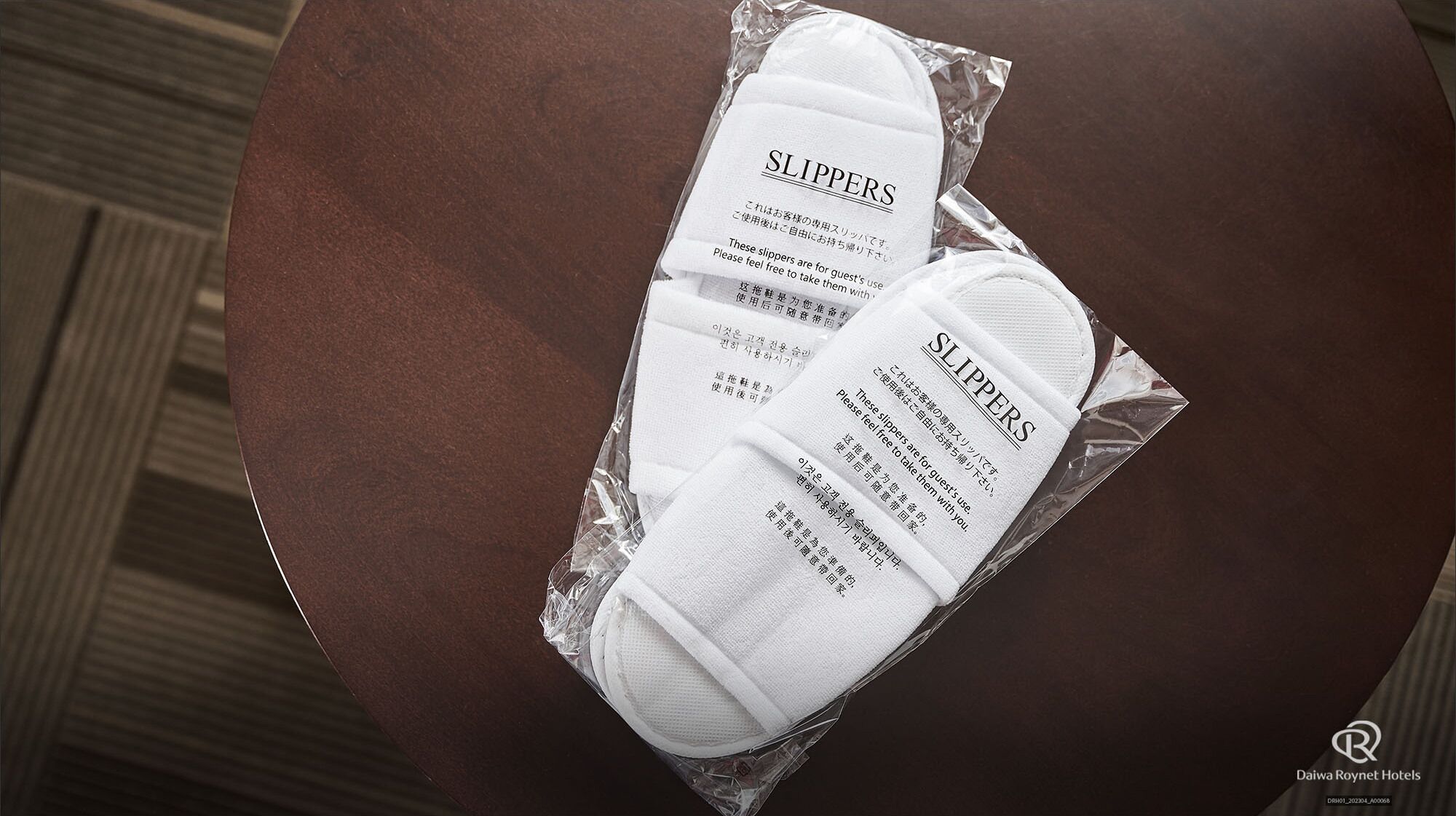 A pair of slippers in a plastic package with a label, placed on a brown surface.