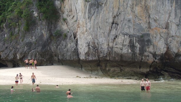 A beach with clear water and a rocky cliff. - Gieng Ngoc Hotel (Hai Phong)