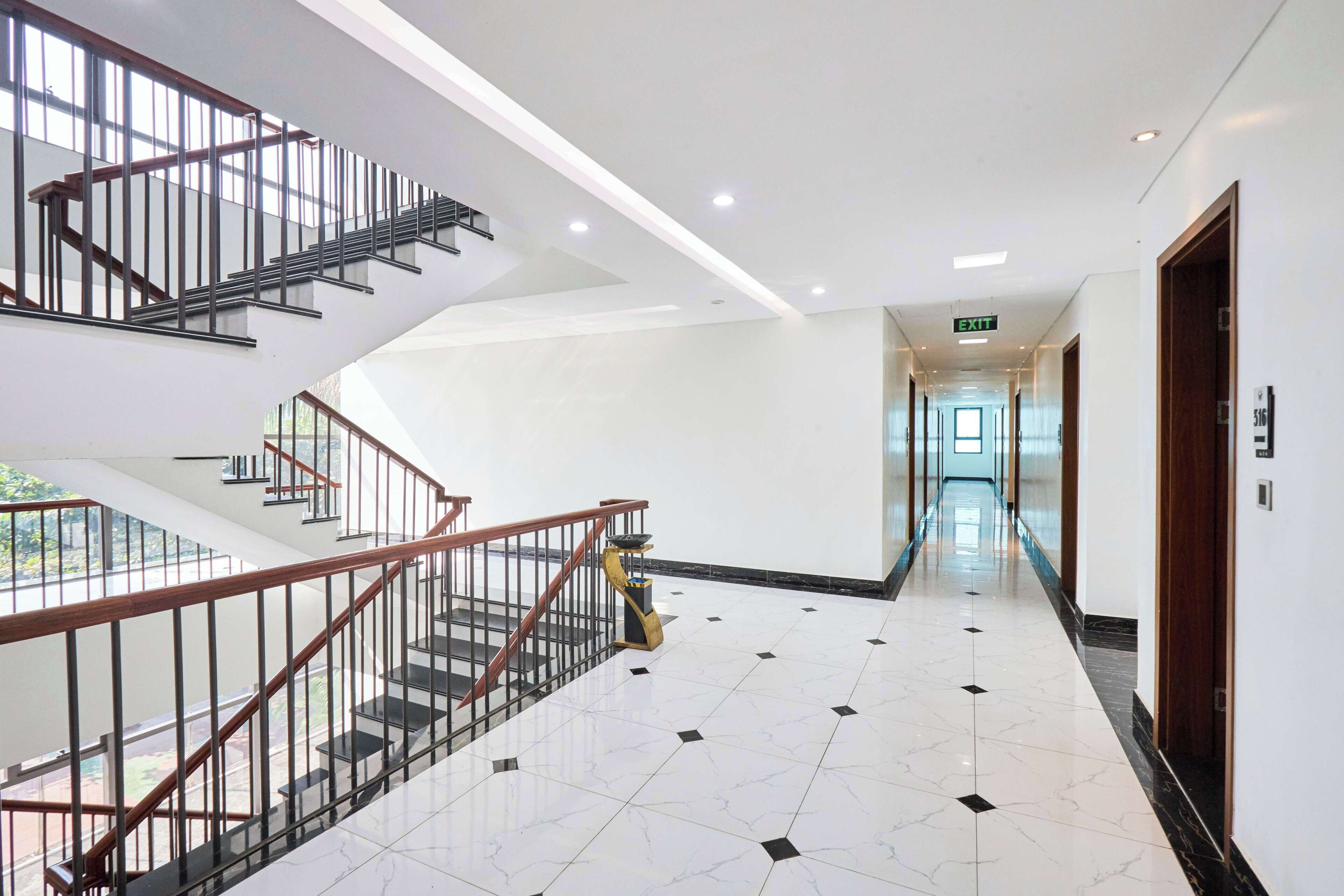 A modern hotel lobby with a central staircase, a clean tiled floor, and a bright exit sign.