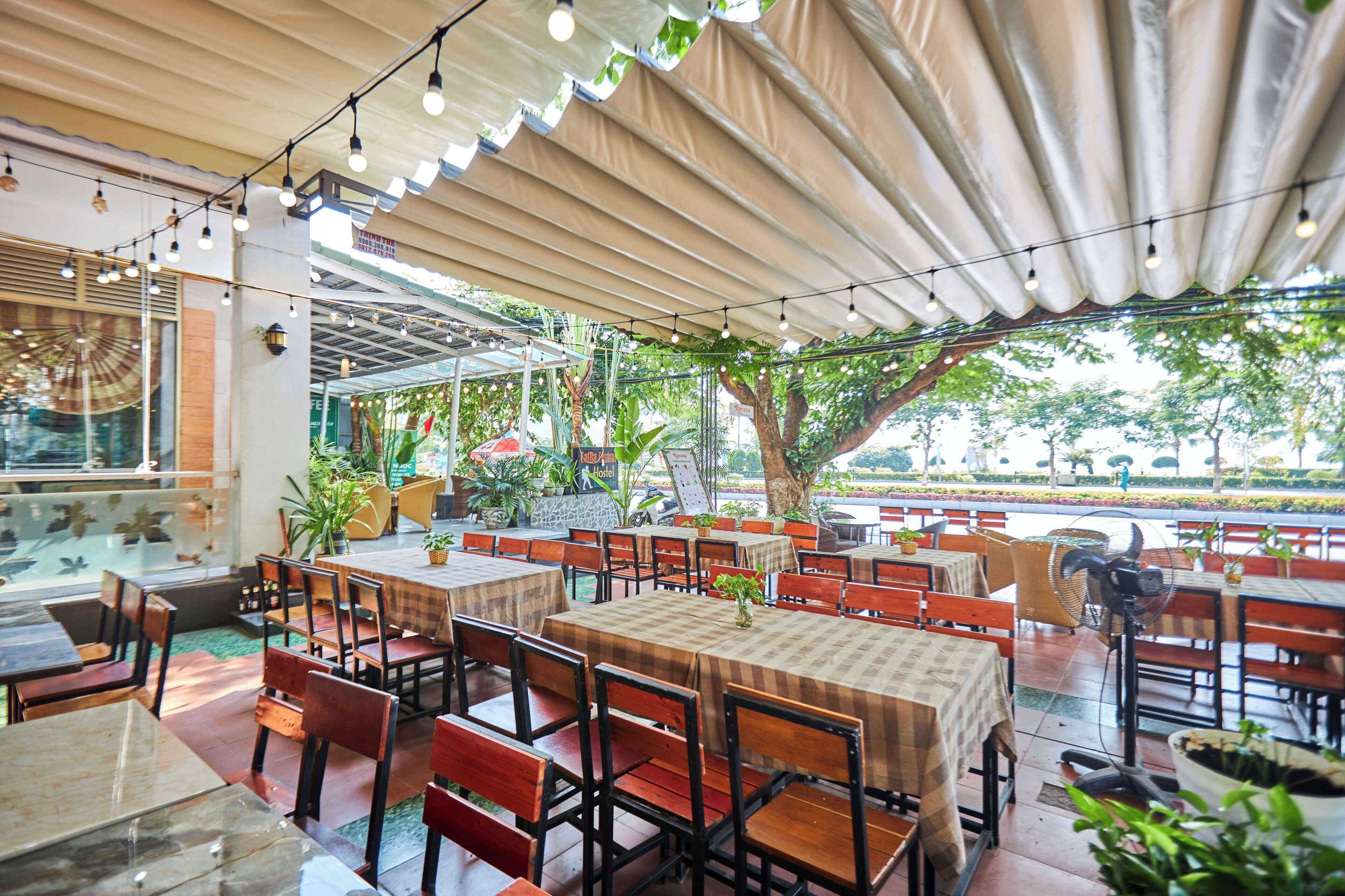 Un espacio de comedor al aire libre con mesas y sillas, cubierto por una estructura y rodeado de vegetación.