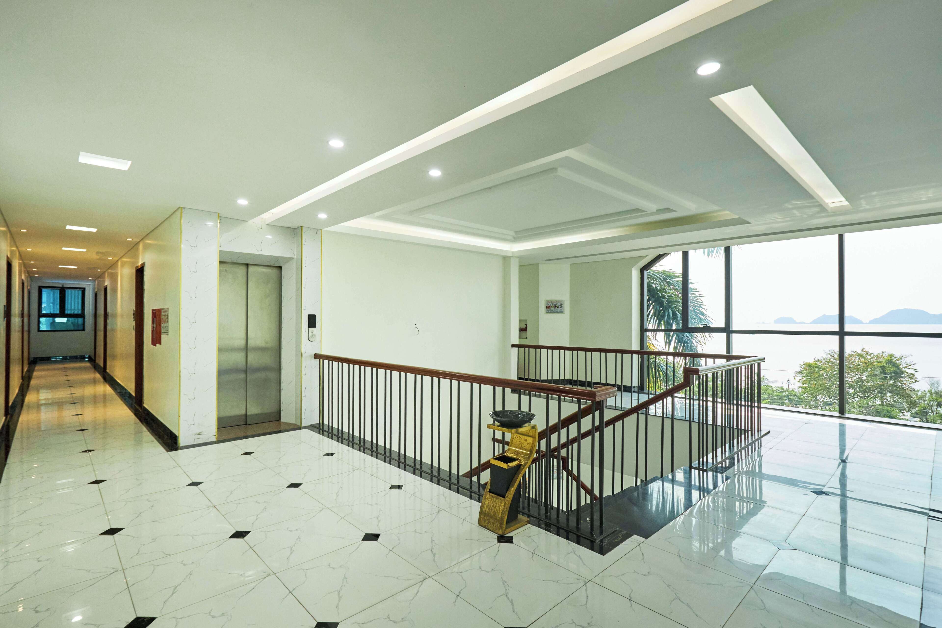A spacious lobby with a marble floor, a staircase with a railing, and large windows offering a view of the outdoors.