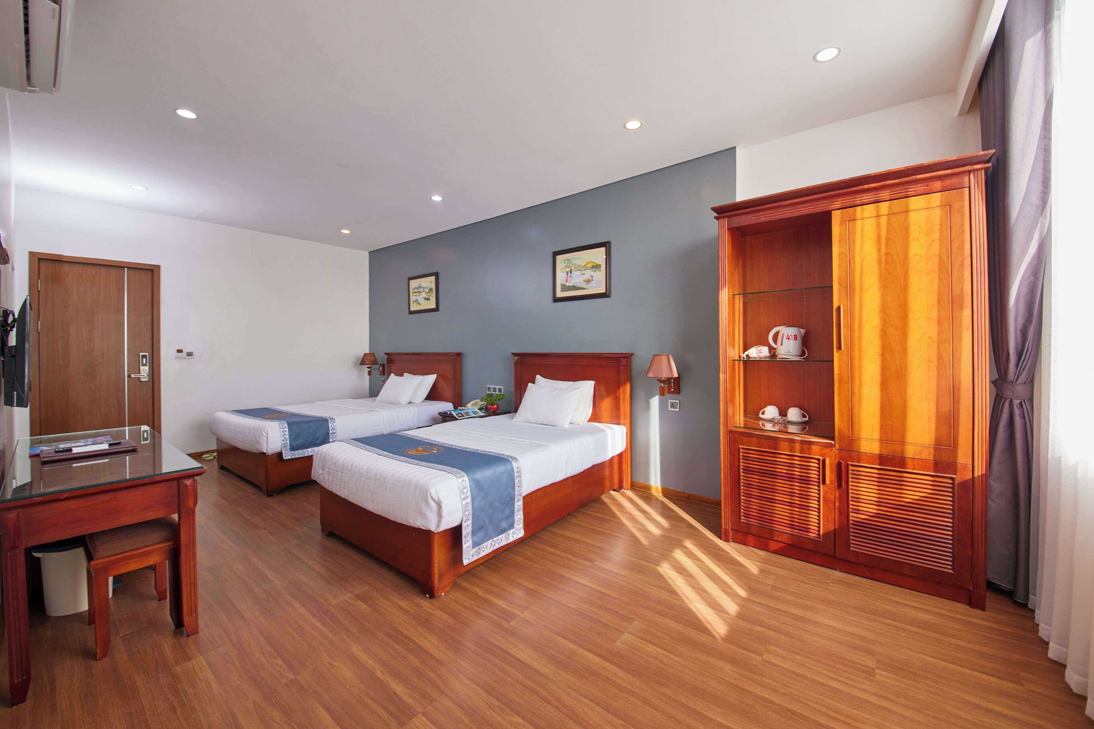 A hotel room with two beds, a wooden wardrobe, a desk, and a small table.