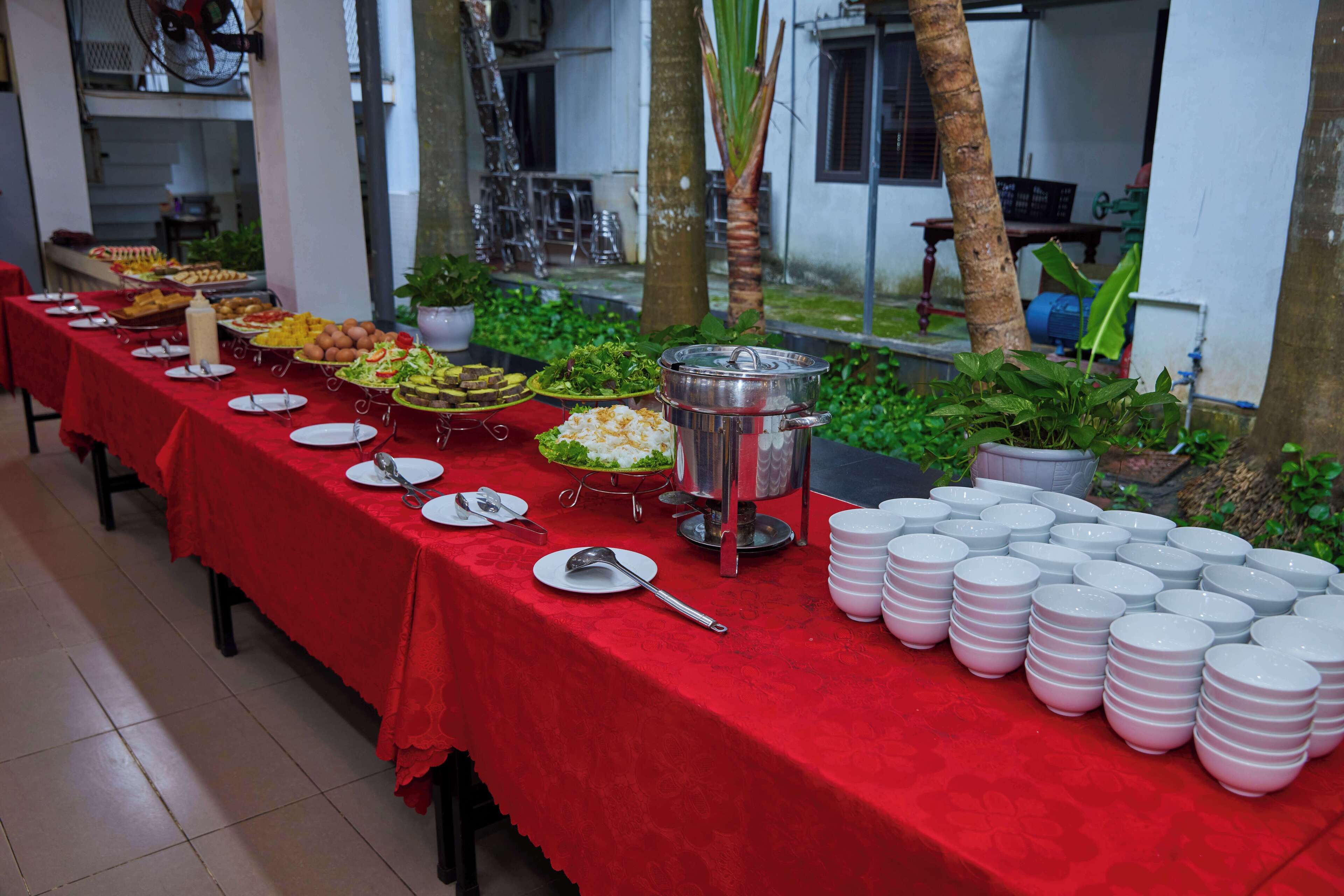 Una mesa de buffet con diversos alimentos y platos, rodeada de pilas de platos y una olla grande.