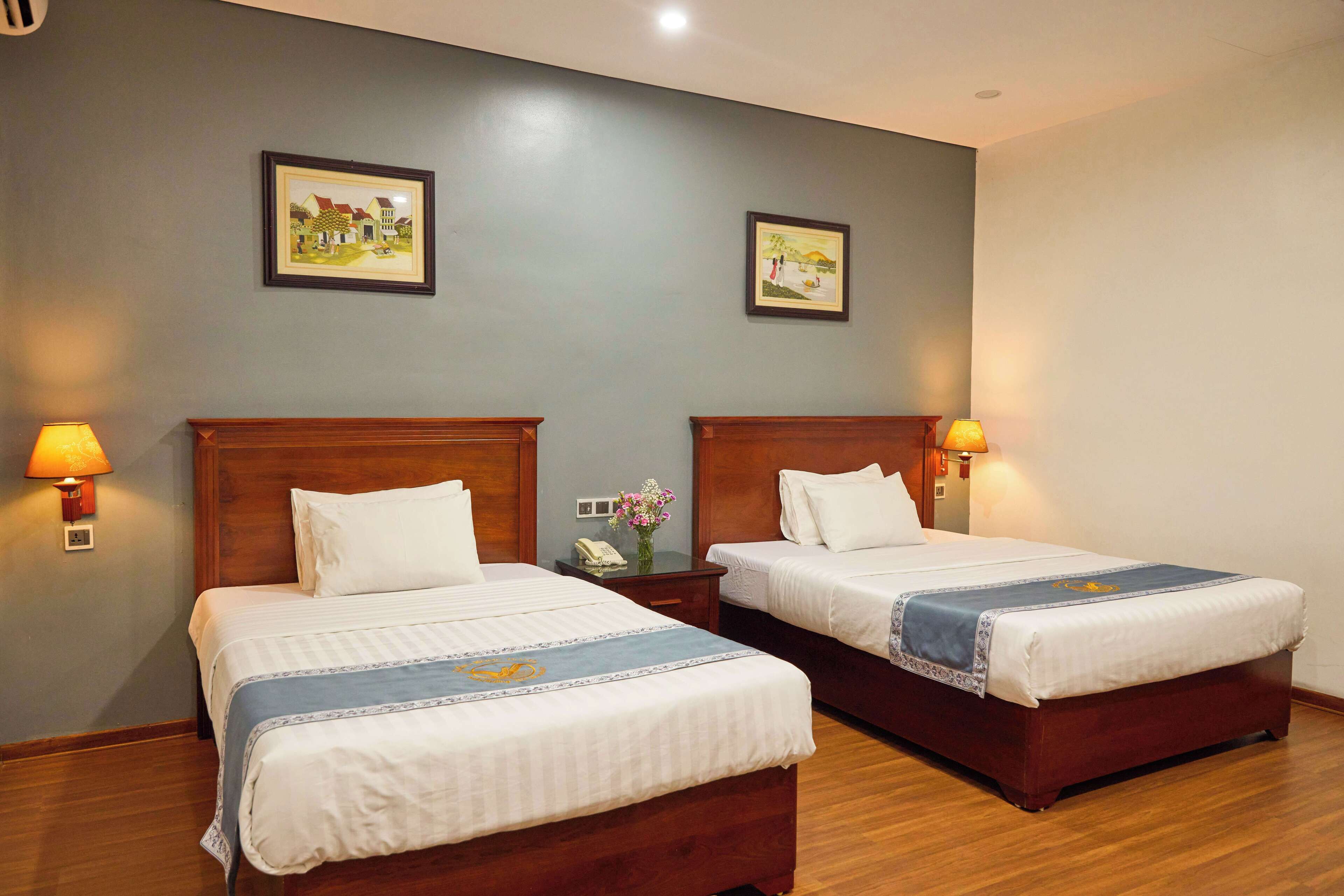 A hotel room with two beds, wooden headboards, and wall-mounted lamps.