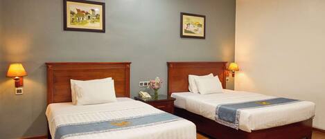 A hotel room with two beds, wooden headboards, and wall-mounted lamps.