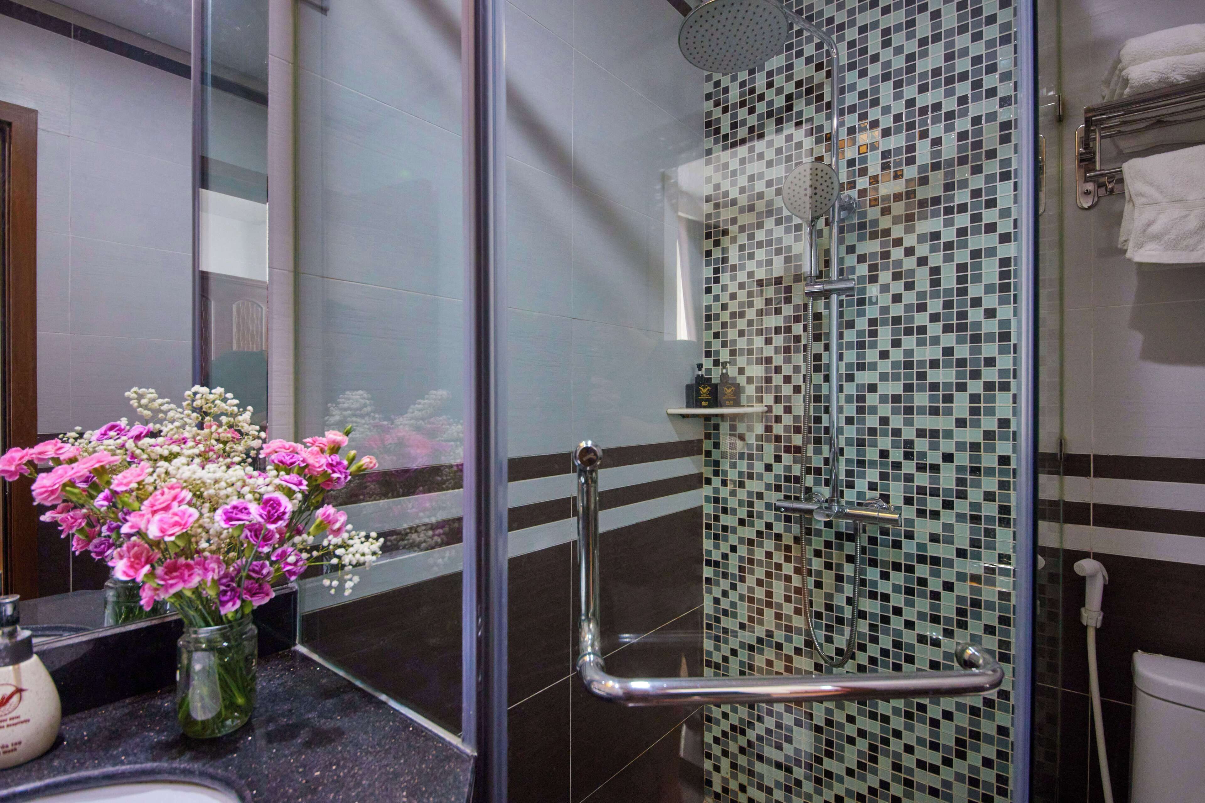 Een badkamer met een glazen douchecabine, een handgreep, een wastafel met een bloemenvaas en een handdoekhouder.