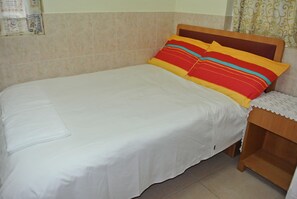 Una cama bien tendida con sábanas blancas y almohadas coloridas a rayas.