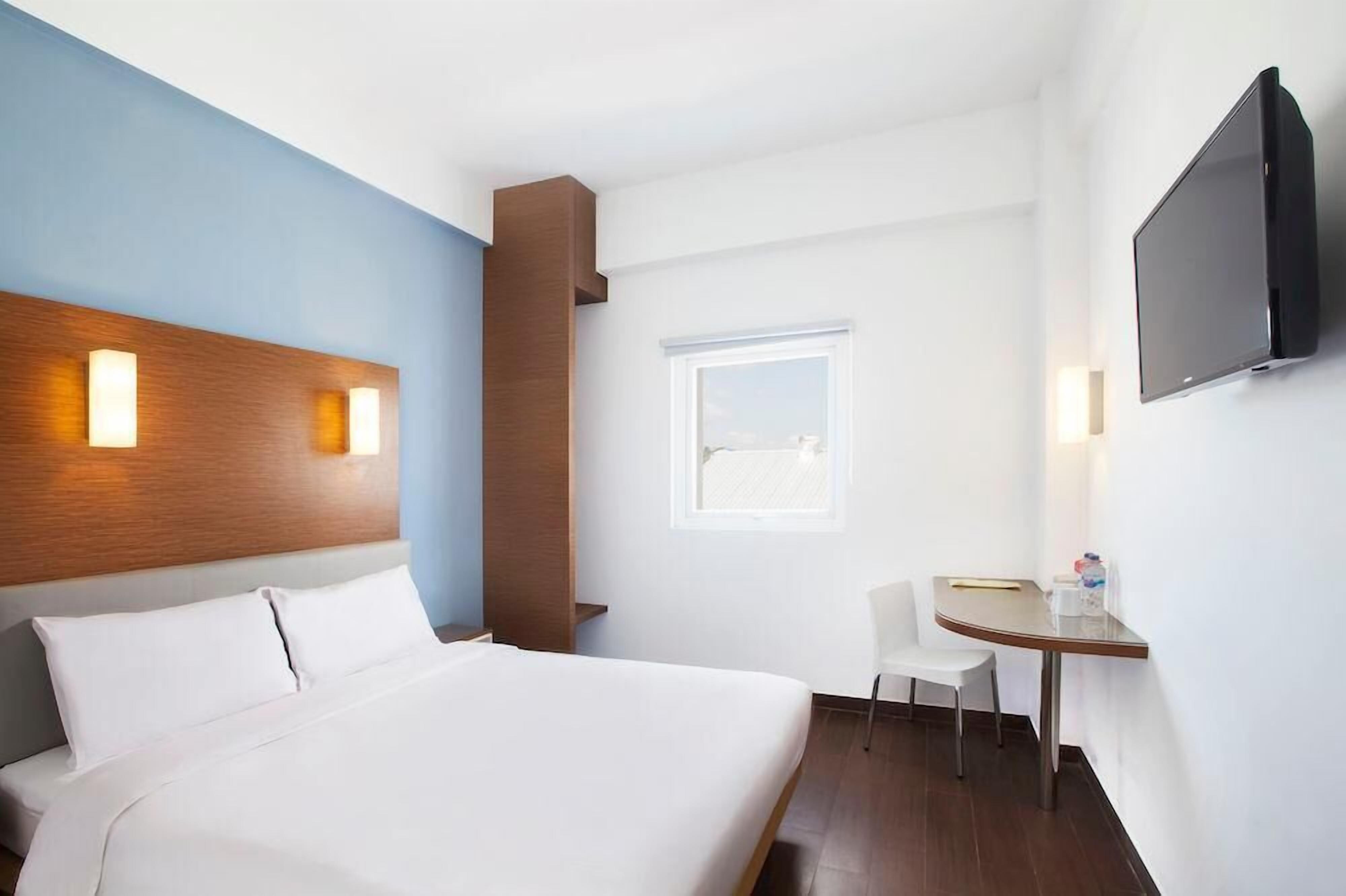 A hotel room with a bed, a desk, a chair, a TV, and a window.