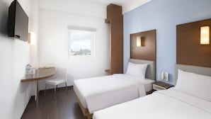 Ett hotellrum med två sängar, ett skrivbord, en stol, en TV och ett fönster med utsikt.