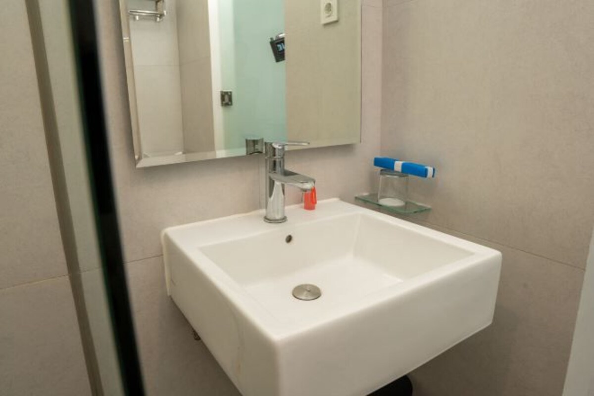 Un lavabo blanc dans une salle de bain, avec un miroir au-dessus, un distributeur de savon et une étagère en verre.