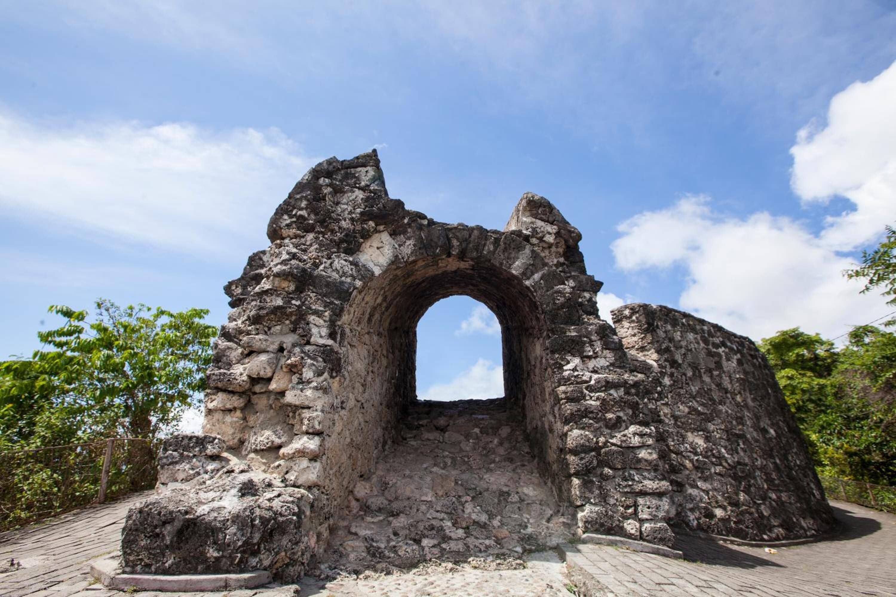 An ancient stone archway with rough, uneven stonework and a cobblestone pathway leading up to it.