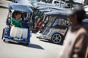 A street scene with a blue and white rickshaw carrying passengers, and a white rickshaw with a logo on the side. - Amaris Gorontalo (Gorontalo)