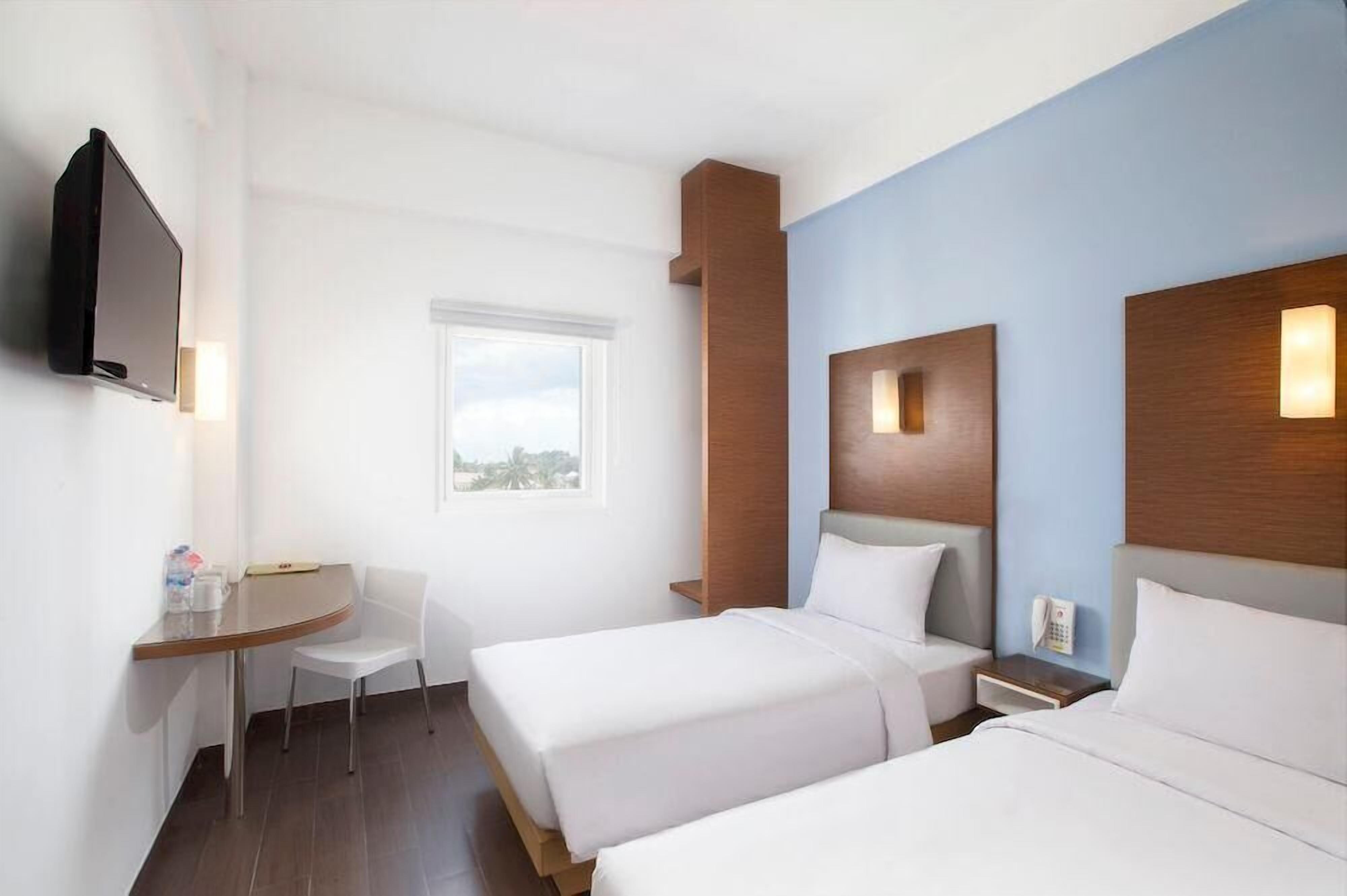 A hotel room with two beds, a desk, a chair, a TV, and a window with a view.