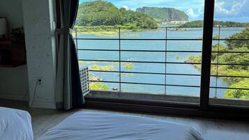 A room with a large window offering a view of a lake, a bed, and a wall-mounted air conditioner.