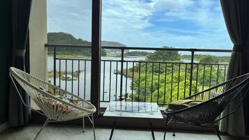 A balcony with two chairs, a glass table, and a view of a river and greenery.
