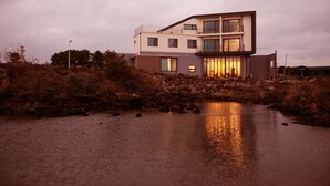 A modern two-story house with a stone bridge over a body of water, reflecting the building's lights. - Maison de Ojolac (Seogwipo)
