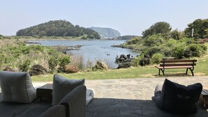 An outdoor seating area with a view of a lake and a distant island. - Maison de Ojolac (Seogwipo)
