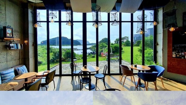 A modern interior with large windows offering a view of a lake and hills. There are seating areas with tables and chairs. - Maison de Ojolac (Seogwipo)