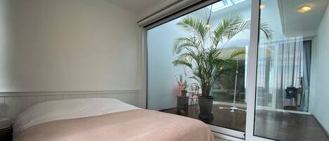 Un dormitorio con una cama, un ventanal corredero que da a un balcón y una planta en maceta.